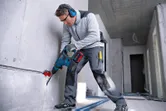 Une personne portant un équipement de sécurité perce du béton avec un marteau perforateur sans fil.
