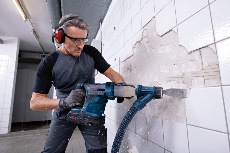 Une personne portant un équipement de sécurité utilise un marteau perforateur sans fil pour retirer des carreaux muraux.