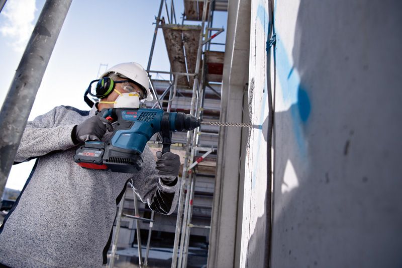 Une personne portant un équipement de sécurité perce un mur en béton sur un chantier de construction.