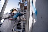 Une personne portant un équipement de sécurité perce un mur en béton sur un chantier de construction.