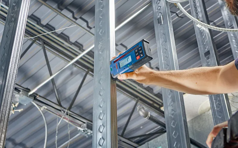 Une personne utilise un récepteur laser pour vérifier l’alignement d’un cadre en acier à l’intérieur.