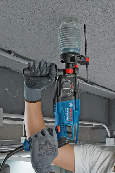 Une personne portant un équipement de sécurité perce un plafond en béton à l'aide d'un outil électrique.