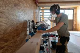 Une personne portant un équipement de sécurité coupe une poutre en bois avec une scie à onglet sans fil.