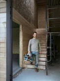 Une personne tenant une scie à onglet se tient sur des escaliers en bois sur un chantier de construction.