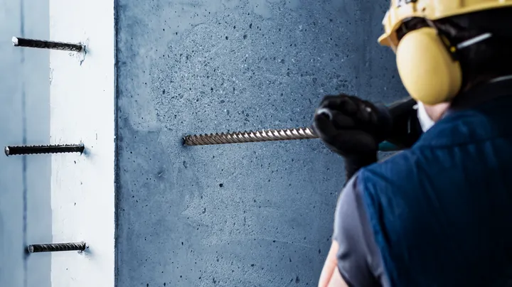Une personne portant un équipement de sécurité perce le béton pour installer des barres d'armature.