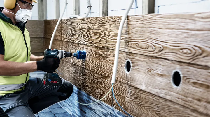 Une personne portant un équipement de sécurité perce un grand trou dans un mur en bois.