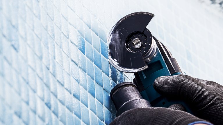 Une personne portant un équipement de sécurité utilise une meuleuse d'angle pour couper des carreaux bleus.