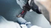Une personne utilise la lame d'un outil multifonction pour couper un tuyau en plastique.