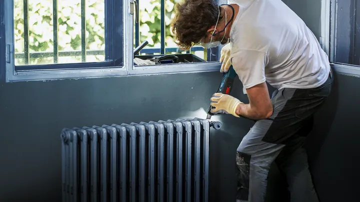 Une personne portant un équipement de sécurité utilise une perceuse sans fil pour installer un radiateur.