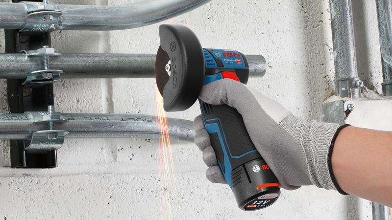 Une personne portant un équipement de sécurité utilise une meuleuse d’angle sans fil pour couper un conduit métallique.