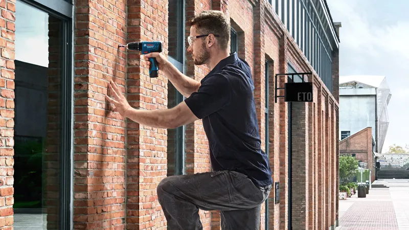 Une personne portant un équipement de sécurité perce un mur de briques à l'extérieur d'un bâtiment.