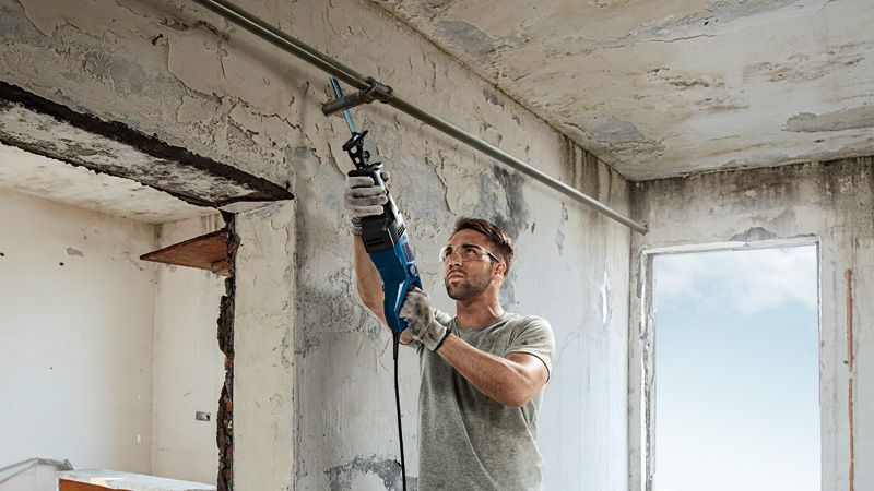 Une personne portant un équipement de sécurité utilise une scie alternative pour couper un tuyau métallique à l’intérieur.