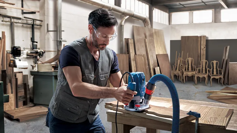Une personne portant un équipement de sécurité utilise une toupie pour façonner le bois dans un atelier.
