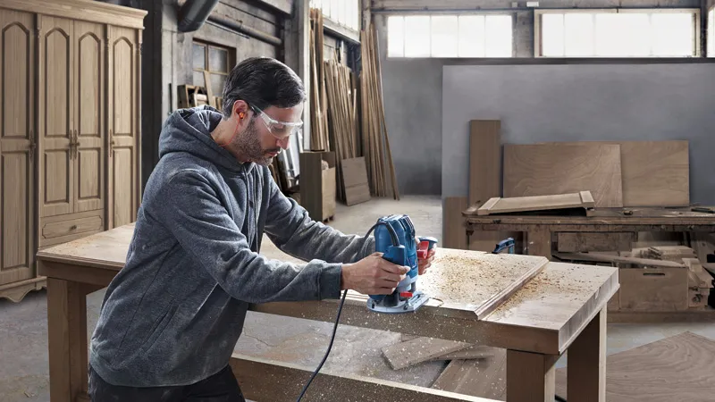 Une personne portant un équipement de sécurité utilise une défonceuse sur une table en bois dans un atelier.