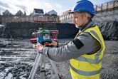 Une personne portant un équipement de sécurité ajuste un outil de nivellement laser sur un trépied sur un chantier de construction.