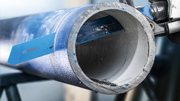 Lame de scie coupant un tuyau métallique épais dans un environnement industriel.