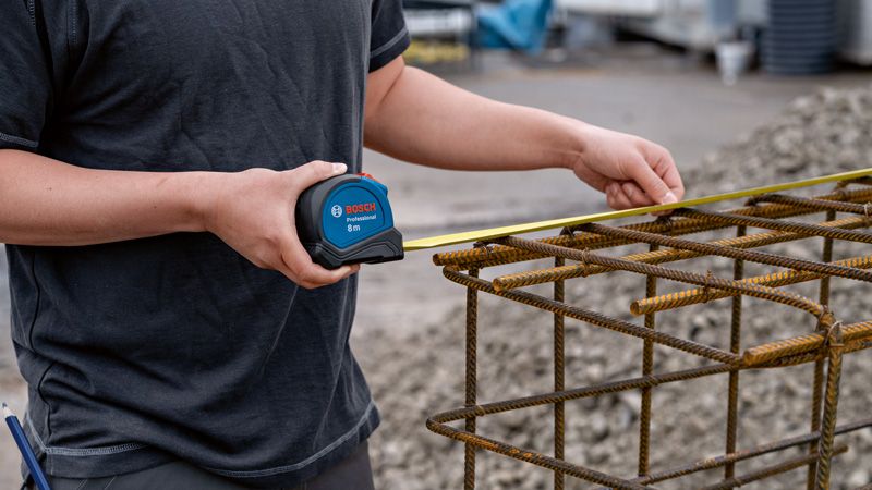 Une personne utilise un ruban à mesurer pour vérifier la largeur d’une structure en barres d’armature métalliques.