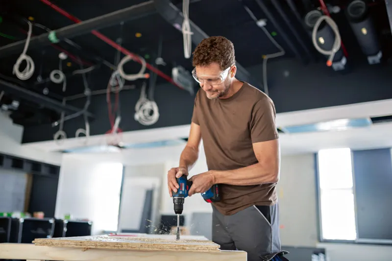 Une personne portant un équipement de sécurité perce du bois sur un chantier de construction.