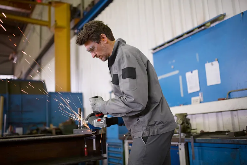 Une personne portant un équipement de sécurité meule du métal, produisant des étincelles dans un atelier.