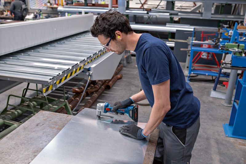 Une personne portant un équipement de sécurité découpe de la tôle sur un établi dans une usine.