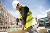 Une personne portant un équipement de sécurité perce du bois sur un chantier de construction.