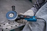 Une personne portant un équipement de sécurité tient une meuleuse d'angle avec disque à lamelles.