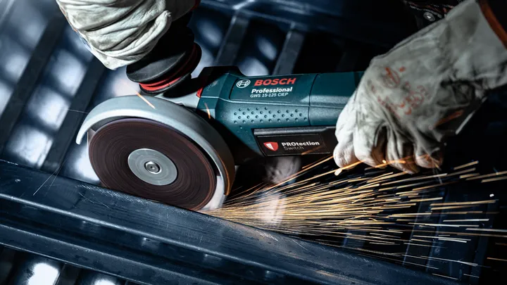 Une personne portant un équipement de sécurité utilise une meuleuse d'angle pour couper le métal, produisant des étincelles.