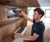 Une personne utilise un tournevis sans fil pour fixer des composants dans un panneau électrique.