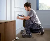 Une personne utilise un tournevis sans fil pour installer un cache de prise électrique.