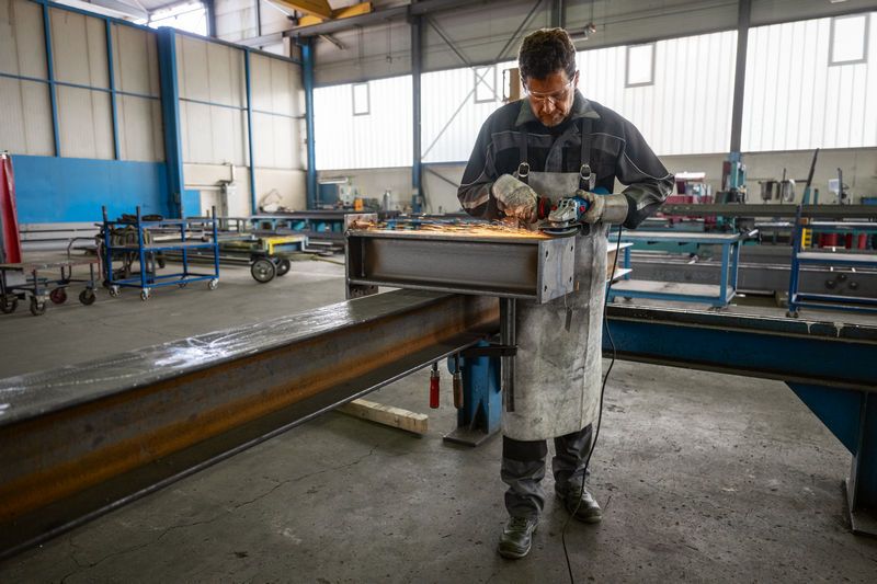 Une personne portant un équipement de sécurité meule une poutre en acier avec une meuleuse d'angle.