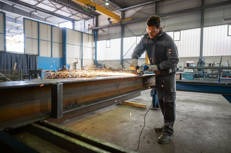 Une personne portant un équipement de sécurité broie une poutre en acier, créant des étincelles brillantes.