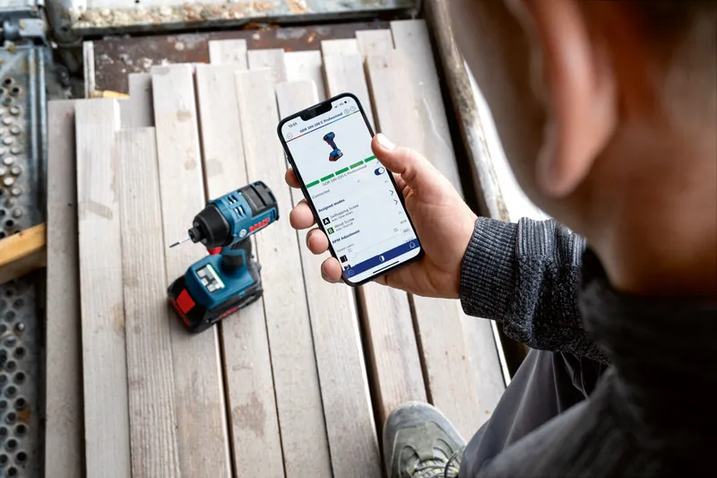 Une personne vérifie les fonctionnalités de l'application d'un outil électrique sur un smartphone à proximité d'une perceuse sans fil.