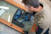 Une personne portant un équipement de sécurité utilise une cloueuse pneumatique sans fil sur un cadre en bois.