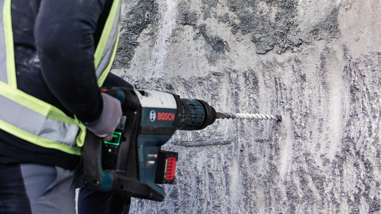 Une personne portant un équipement de sécurité perce un mur en béton avec un outil électrique.