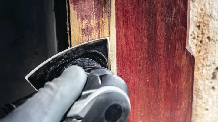 Une personne portant un équipement de sécurité ponce un cadre de porte en bois avec un outil électrique.