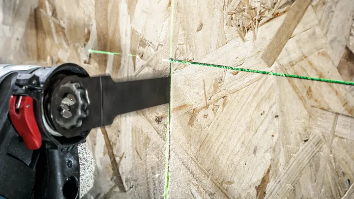 Une personne portant un équipement de sécurité utilise une scie alternative pour couper du bois le long d’une ligne directrice verte.