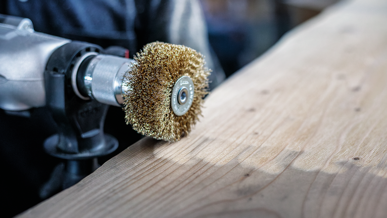 Une personne utilise une brosse métallique pour nettoyer une surface en bois.