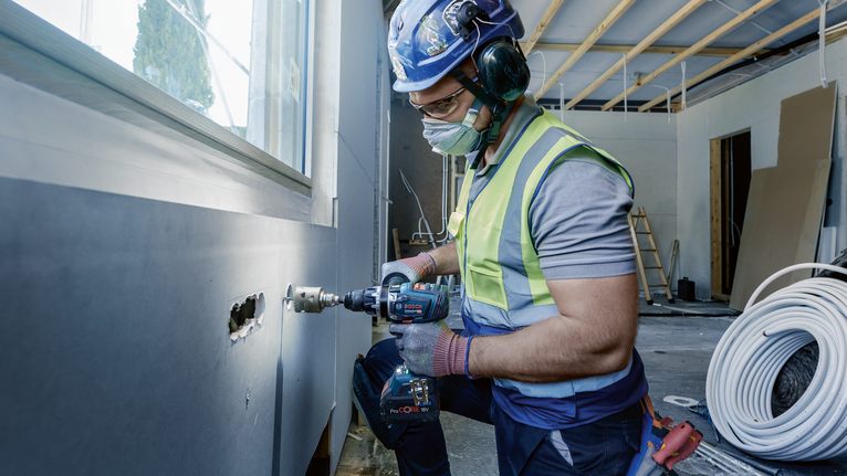 Une personne portant un équipement de sécurité perce un trou dans un mur sur un chantier de construction.