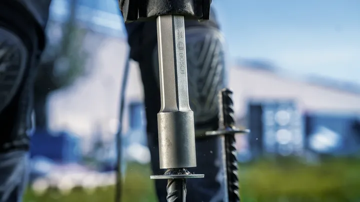 Une personne portant un équipement de sécurité utilise un outil électrique pour enfoncer une tige dans le béton.