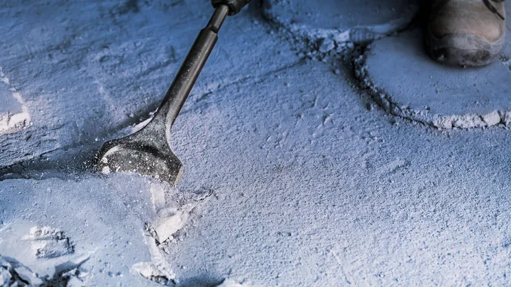 Une personne portant un équipement de sécurité cisèle une surface en béton.