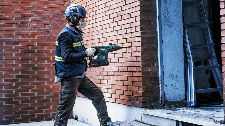 Une personne portant un équipement de sécurité perce un mur de briques près d'une porte.
