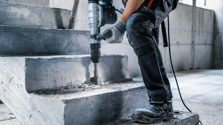Une personne portant un équipement de sécurité utilise un marteau perforateur pour briser des escaliers en béton.