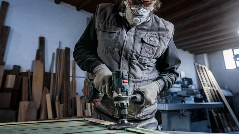 Une personne portant un équipement de sécurité polit du bois avec un outil électrique dans un atelier.