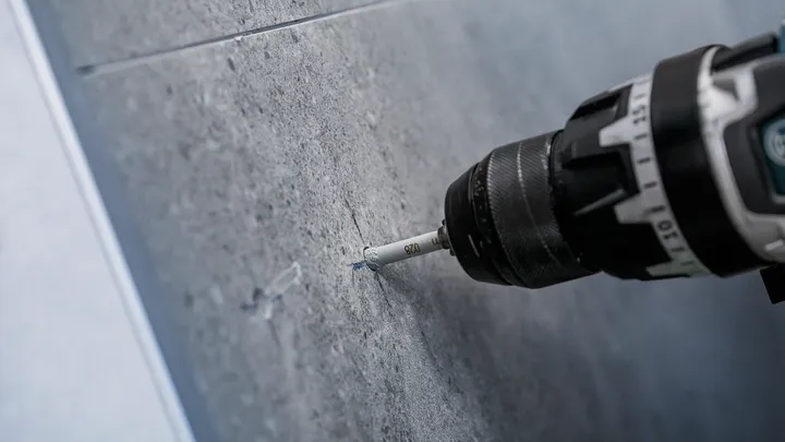 Une perceuse faisant un trou précis dans un mur carrelé gris.