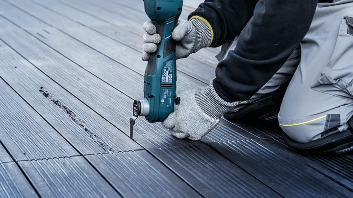 Une personne portant un équipement de sécurité utilise un outil électrique pour découper des rainures dans une terrasse en bois.