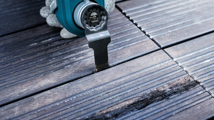 Une personne portant un équipement de sécurité utilise un outil électrique pour couper une terrasse en bois.