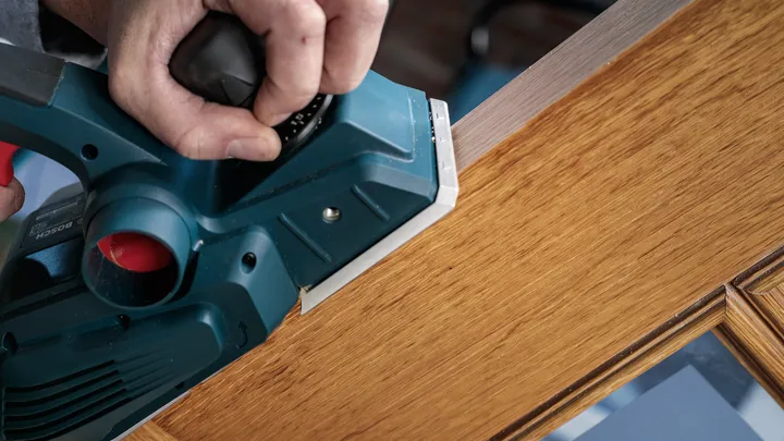 Raboteuse électrique lissant le bord d'une porte en bois.