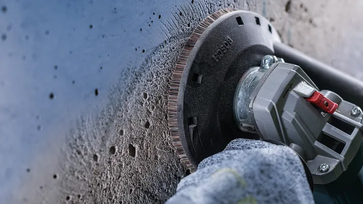 Une personne portant un équipement de sécurité utilise une meuleuse d'angle pour lisser un mur en béton.