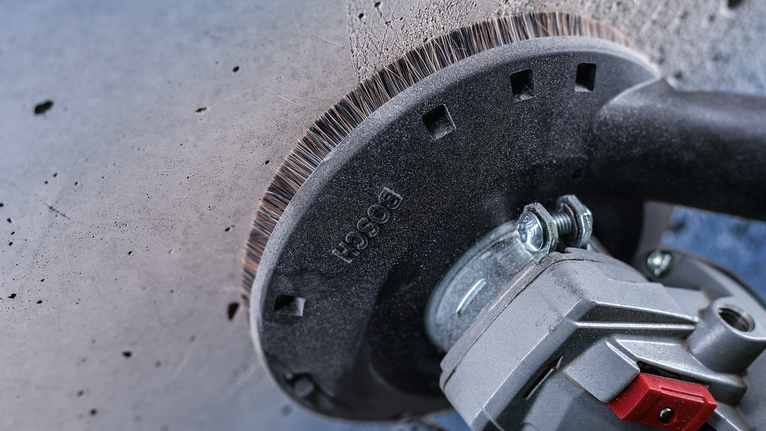Une brosse métallique fixée à un outil électrique nettoie la surface d'un mur en béton.