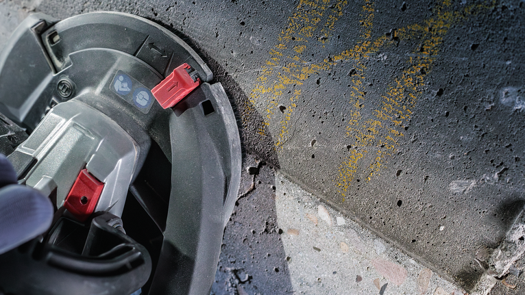 Une personne portant un équipement de sécurité utilise une scie circulaire pour couper une surface en béton.